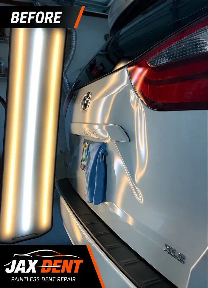 Dent in the rear liftgate of a white minivan under PDR lighting, before repair