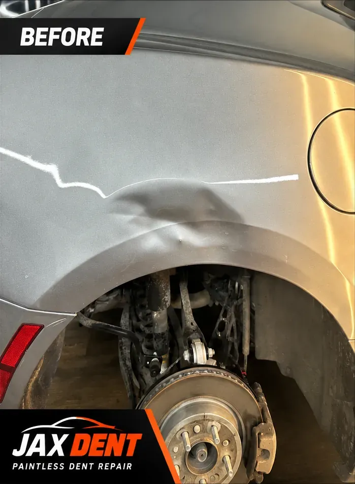 Dent in the rear quarter panel of a silver sedan with the wheel removed, before repair